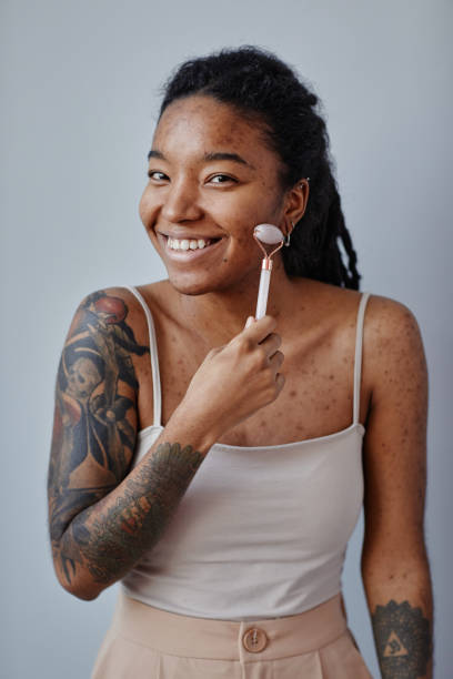istock Young black woman with acne scars and tattoos using face massager and smiling 1463321964