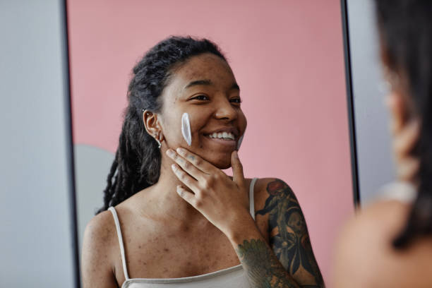 istock Candid smiling black woman with acne scars using face cream by mirror 1463321974