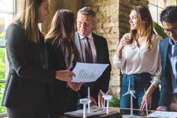 istock Young entrepreneurs talking about renewable energy project standing around a table holding data paperwork 1463337002