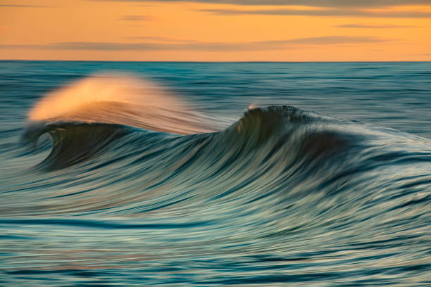 Smooth ocean wave forming in early morning golden light and dramatic sky at sunrise