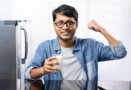A happy Indian male with glass of milk on white background