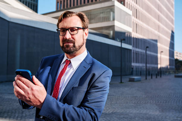 istock Businessman looking at the camera while using a mobile outdoors 1463345834