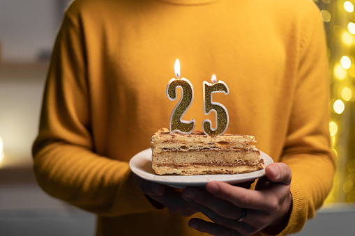 Cake with the number 25 lighted candles in men hands. 25th birthday concept