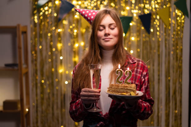 birthday celebration. caucasian girl makes a wish closing her eyes holding a birthday cake with candles number 22 in her hands. - 21e verjaardag stockfoto's en -beelden