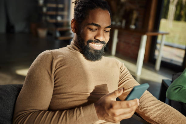 istock Happy black man text messaging on cell phone at home. 1463347886