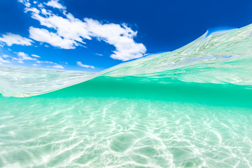 Split image of crystal clear blue water at the beach and a sunny blue sky day.
