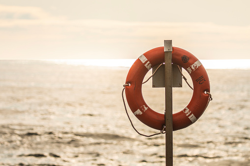 Orange emergency life saving flotation ring on the coastline with bright sunrise in background