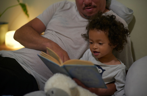 Black family, night and story with child in bed for bonding, care and learning development. Dad, toddler and reading fairytale or education book with daughter for bedtime routine in home