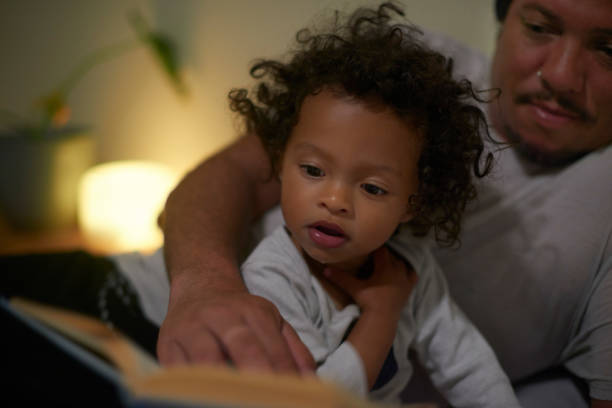 Night, story and curious child in bedroom for bonding, care and learning development with father. Dad, black family and reading fairytale or education book with daughter for home bedtime routine.