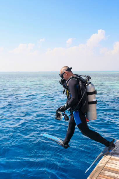 Middle aged Athletes  handsome men scuba divers ready for scuba diving,  jumping in   Beautiful tropical blue sea, coral reef  in the background. Water sports. stock photo