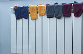 Multicolored socks drying on the white radiator in the room. Heating season.