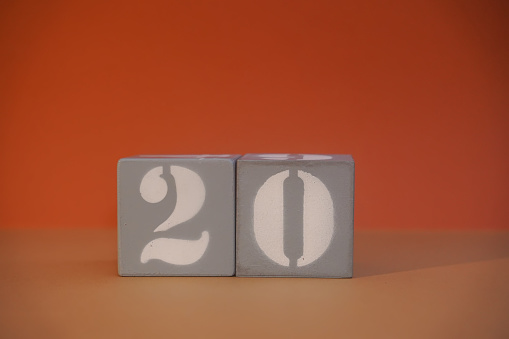 Number 20 on wooden grey cubes close-up. Concept of date time. Math concept. Copy space for text or event. White numbers 20 on building blocks, orange background. Selective focus, blurred background
