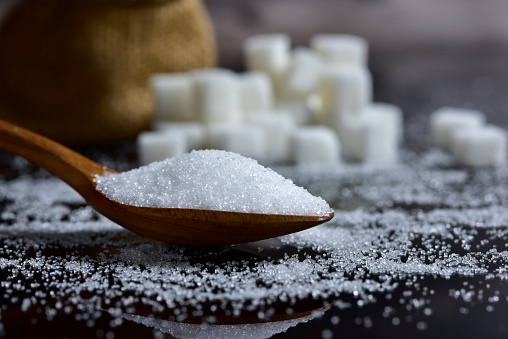 Closeup sugar piling up the shape of the hill from wooden spoons and sugar cubes on a black background. selective focus.