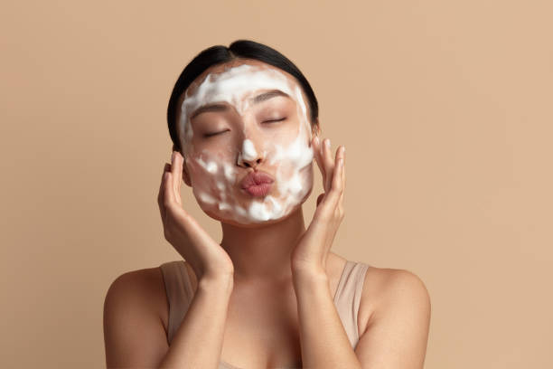 cura della pelle del viso. donna asiatica divertente che pulisce la pelle del viso con sapone di schiuma - lavarsi il viso foto e immagini stock