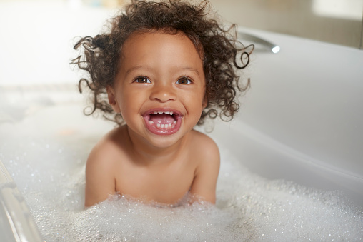 Bathtub, happy kids and girl laughing in water, soap and foam for washing, hygiene and fun at home. Children, shower bubbles and smile in bathroom for health, wellness and skincare cleaning in house