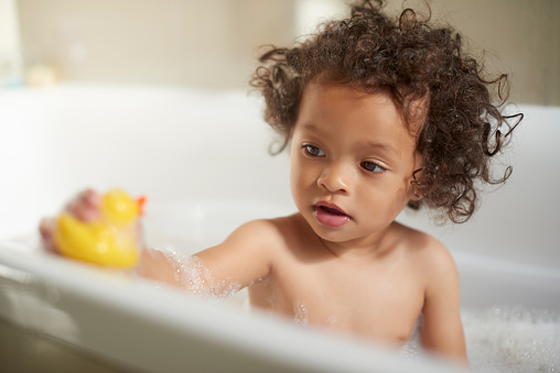 Fun, playful and a baby in the bath with toys for playing, cleaning body and routine. Hygiene, focus and child in a bubble water for washing, bathing and clean grooming in a home bathroom with a duck