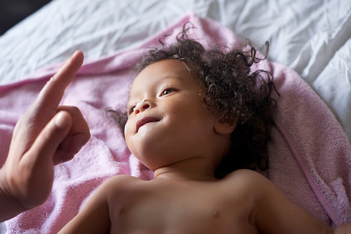 Playful, care and child looking at mother for love, relax and calm during morning grooming routine. Family, carefree and baby playing on a bed with the hand of a parent after waking up in a bedroom