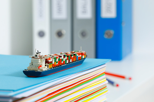 Model of a container ship on an office shelf with a row of folders in the background