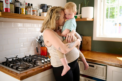 Family, love and children with a woman and boy hugging while standing in the kitchen of their home together. Kids, hug and trust with a woman and male son embracing while bonding in a house