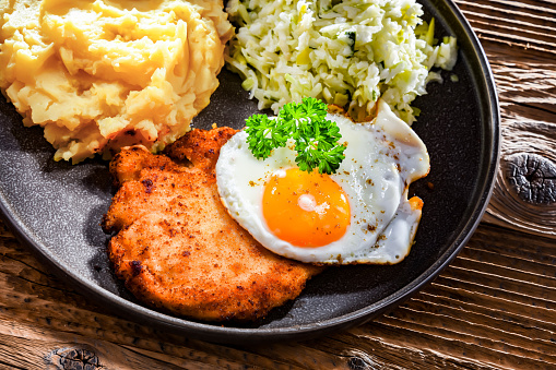 Breaded chicken cutlet served with fried chicken egg, potatoes and cabbage
