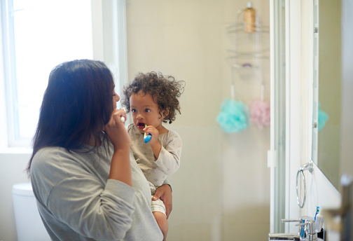 Dental, health and mother with baby brushing teeth in bathroom, learning and cleaning in their home. Oral hygiene, child development and mom teaching child about mouth, teeth and grooming together