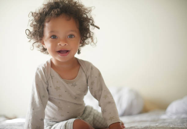 Portrait, baby and bedroom with a girl child sitting on a bed in her home wearing pajamas in the morning. Children, toddler and mockup with a female kid in a house to relax after waking up early stock photo