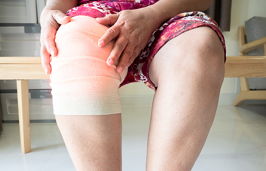Middle aged adult woman suffering from arthritis disease and  wearing elastic support knee. Women touching on knee, Osteoarthritis.