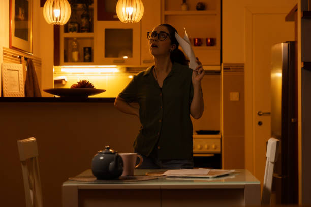 istock Young thoughtful Caucasian woman with glasses holds documents while standing in kitchen. Concept of overdue taxes, layoffs and unexpected bad news 1463369088