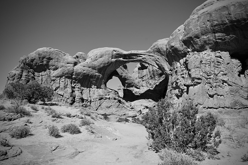 A landscape grayscale scene of Double O Arch in Arches National Park under gray sky