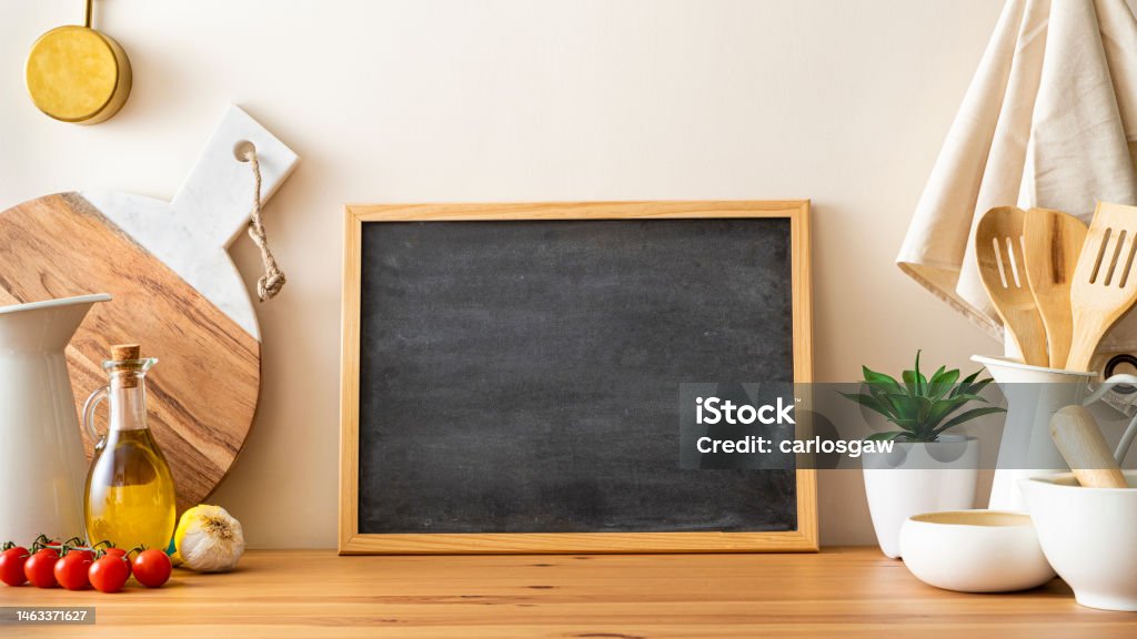 Kitchen countertop with copy space on a blackboard Front view of a kitchen wooden table top with culinary utensils and mediterranean ingredients at the borders of the image leaving a useful copy space at the center on an empty blackboard. Predominant colors are brown and beige. Table Stock Photo