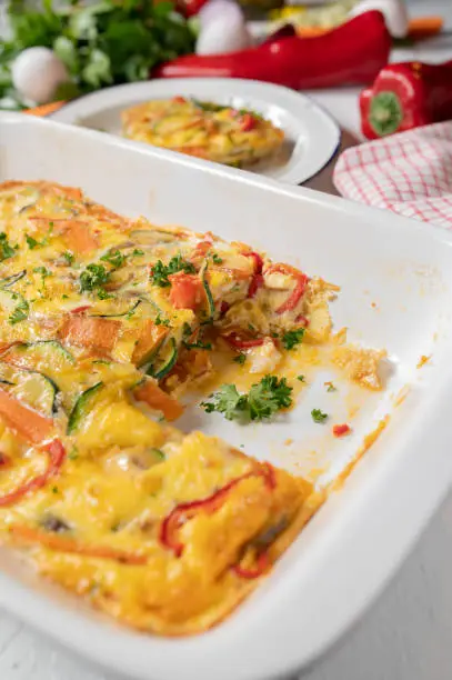 Oven baked frittata with mediterranean vegetables in a white baking dish on kitchen table. Meal for breakfast, lunch or dinner. Suitable for Low carb or ketogenic diet