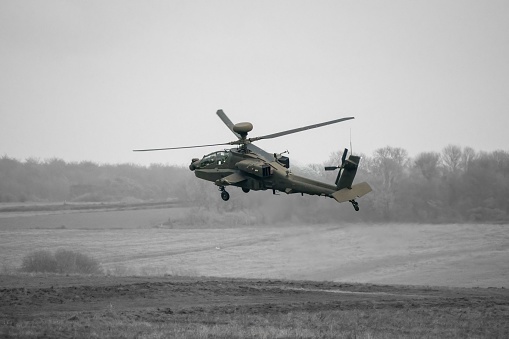 A dark grey army attack helicopter in very low level flight