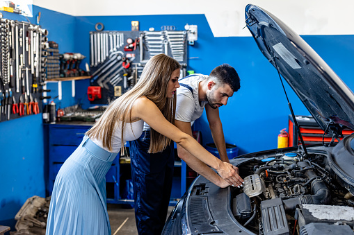 A Car Mechanic is Working on the Car Engine in a Car Service and Trying to Explain a Failure to a Female Customer.