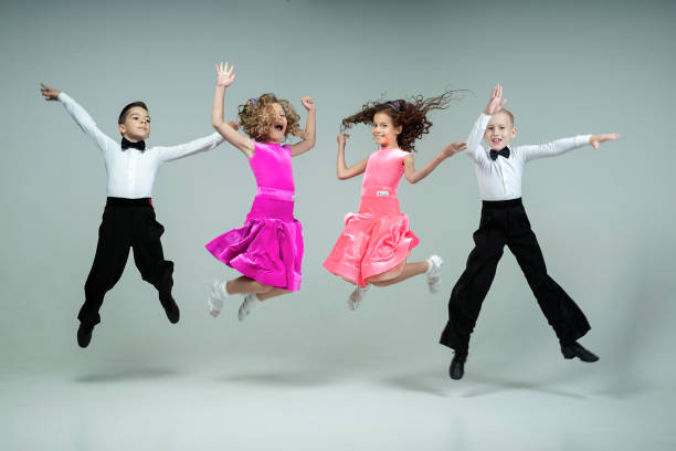 巻き毛の女の子2人と男の子2人が社交ダンスを笑い、いたずらっぽく飛び上がる - powerful owl ストックフォトと画像