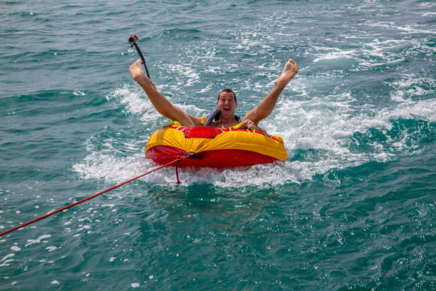 istock Man sitting in an inflatable ring towed by a boat and holding a camera 1463378911