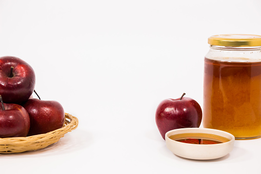 A closeup shot of a Pile of apples, a red apple, and a jar and bowl of honey isolated on a white background. Symbols of Jewish New Year-Rosh Hashanah.