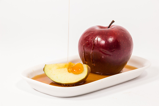 The pouring honey on red apple and red apple slice on a white plate with honey isolated on a white background.