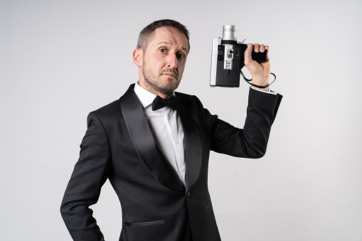 Man in an elegant suit handling a Super 8 camera in classic secret agent pose.