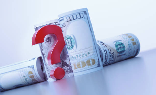 Rolled up 100 American Dollar bills and red question mark over grey background. Horizontal composition with copy space. Finance concept.