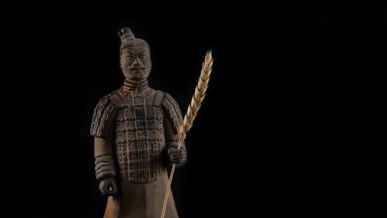 A copy of the terracotta soldier of the army of Emperor Qin Shi Huang with an ear of wheat in his hand on a black background