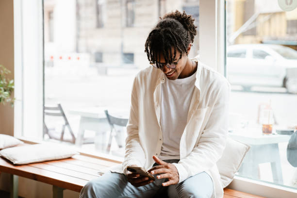 istock Young african american man smiling and using cellphone in cafe indoors 1463382466