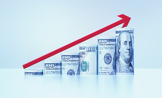 Rolled up 100 American Dollar bills and a red arrow forming a bar graph over grey background. Horizontal composition with copy space. Finance concept.