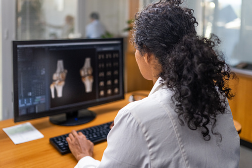 Female doctor examining medical x-rays on computer monitor in hospital.