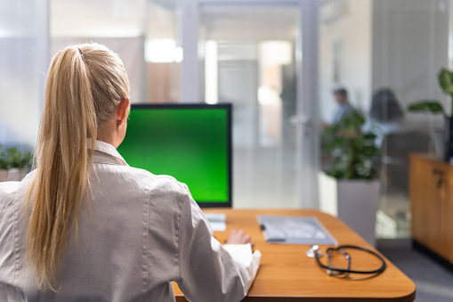 Female doctor looking at green screen of computer monitor in hospital.