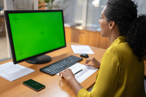 Woman looking at green screen of computer monitor in office.