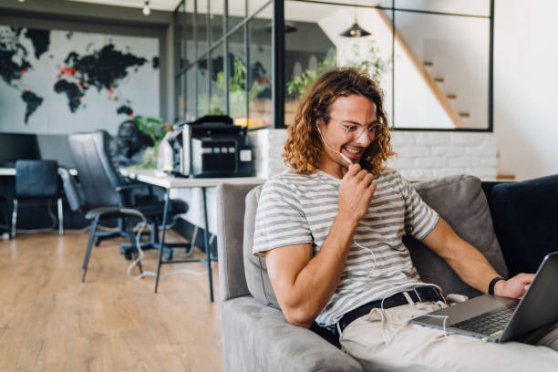 istock Young man using laptop and earphones while sitting on sofa in office 1463384568