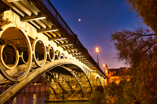 Night photo of the Triana bridge with streetlights and reflections in the water, Seville,Andalusia, Spain.