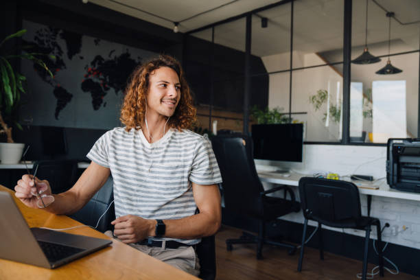 istock Young man using laptop and earphones while sitting by table in office 1463385247
