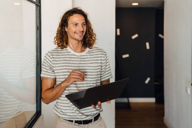 istock Young curly man using laptop and earphones while working in office 1463385431