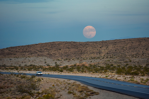 Southwest desert landscape with a full moon and a Jeep on the mountain pass